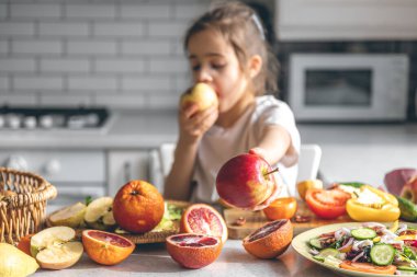 Funny little girl appetizingly eats apples in the kitchen, health and nutrition concept.