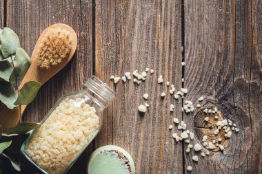 Fırça, deniz tuzu, sabun ve kurumuş çiçekler, ahşap arka planda, düz uzanmış.