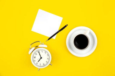 Alarm saati, bir fincan kahve ve kağıt sarı arka plan, düz yatak, iş konsepti.