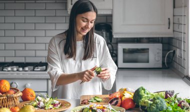 Attractive young woman cutting vegetables for salad in the kitchen, food preparation concept.