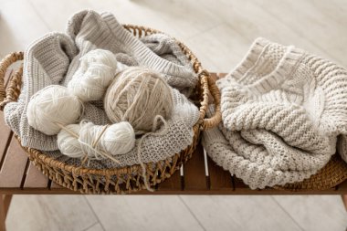 Basket with threads for knitting on a wooden bench in the interior of the room, the concept of knitting. clipart