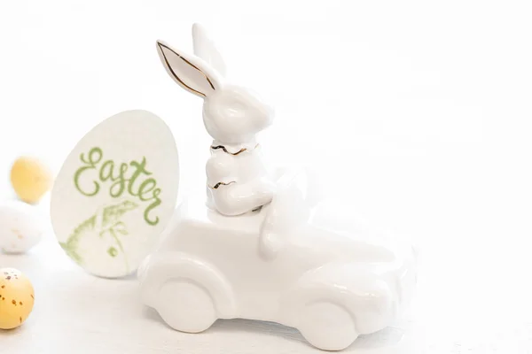 Easter background with a ceramic hare in the car and Easter eggs on a white background,
