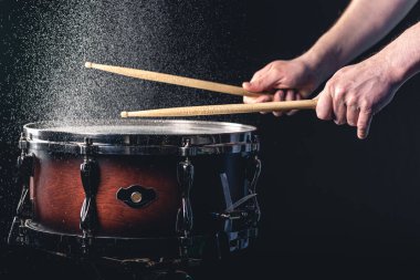 Davulcu davul çubuklarıyla davula vuruyor. Siyah arka planda su sıçratıyor..