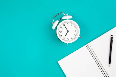 Mavi arkaplan üzerinde not defteri ve alarm saati, düz uzanma, kopyalama alanı.