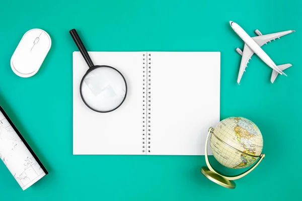 Flat lay composition with notebook, globe, airplane and magnifier on blue background, tourism and geography concept, copy space.
