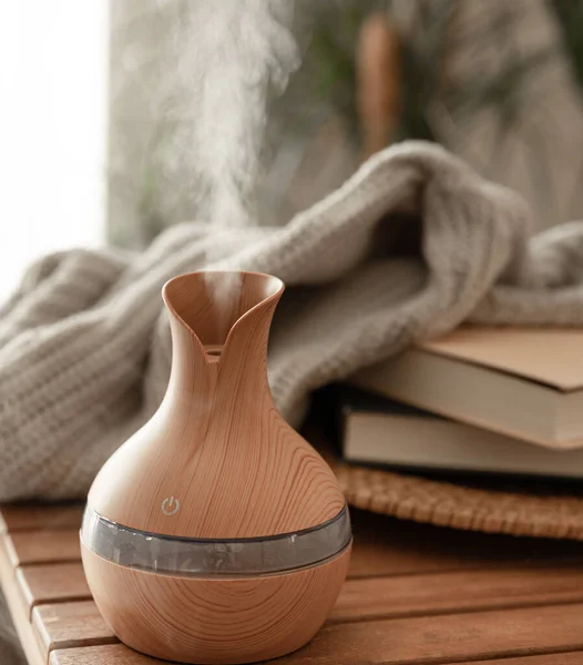 stock image Aroma oil diffuser lamp on blurred background with books and knitted element.