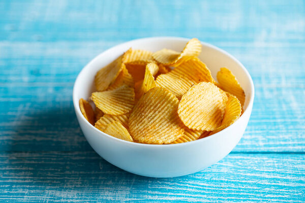 Крупный план, тарелка картофельных чипсов на размытом голубом деревянном фоне.