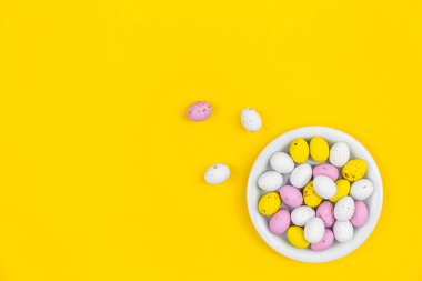 Sarı zemin üzerinde renkli Paskalya yumurtaları olan tabak, üst görünüm, minimalizm, kopyalama alanı.