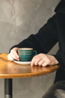 Bir fincan cappuccino. Tahta bir masanın üzerinde. Sabahları bir kafede erkeklerin elinde..