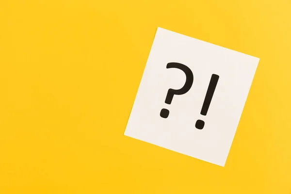 Question mark and exclamation mark on paper on yellow background, flat lay.