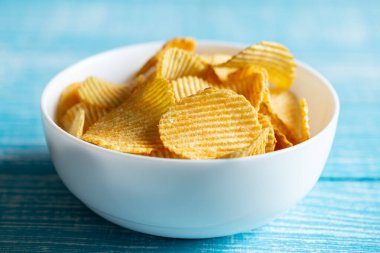 Yakın plan, bulanık mavi ahşap arka planda bir tabak patates cipsi..