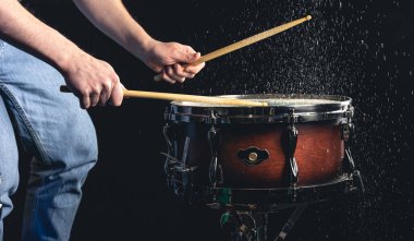 Davulcu davul çubuklarıyla davula vuruyor. Siyah arka planda su sıçratıyor..