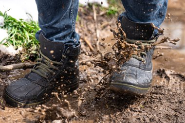 Kot pantolon ve bot giyen bir adam yağmurlu havada, kırsalda, bacakları kapalı bataklıkta yürür..
