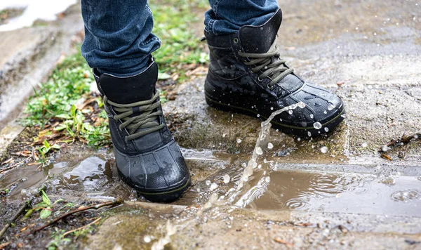 A pair of durable mens boots, a man in quality shoes stands on gravel, quality waterproof boots for bad weather, close-up.