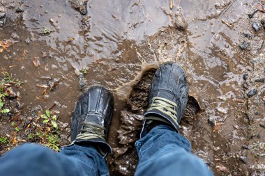 Yukarıdan bakıldığında çamurda bir çift yürüyüş ayakkabısı, kot ve bot giyen bir adam yağmurlu havada bataklıkta yürür, kapanır.