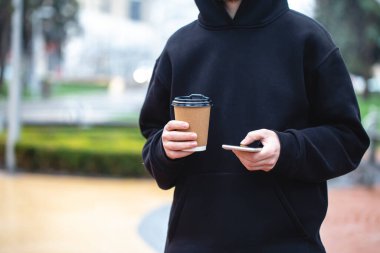 Bir adam elindeki kağıt bardakla akıllı telefonu bulanık bir arka planda, Gadget yakın plan, kullan-at kağıt bardak....