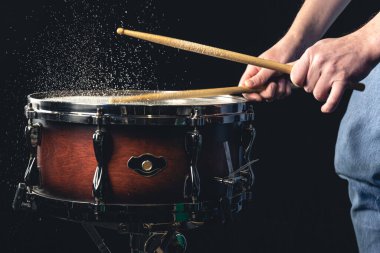 Davulcu davul çubuklarıyla davula vuruyor. Siyah arka planda su sıçratıyor..