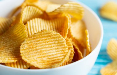 Yakın plan, bulanık mavi ahşap arka planda bir tabak patates cipsi..