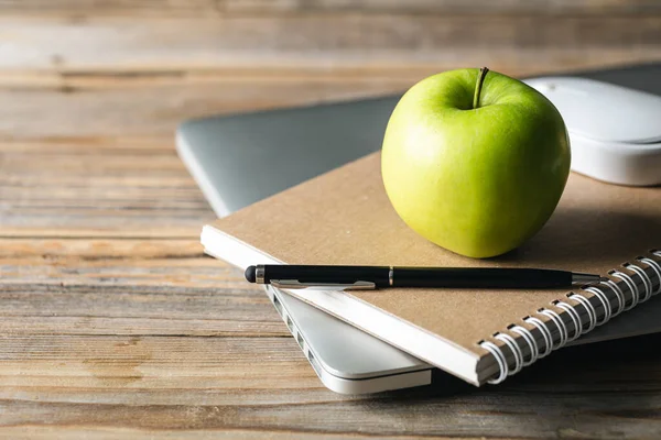 Apple, notepad and laptop on desktop, healthy snack at work or school.