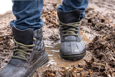 Kot pantolon ve bot giyen bir adam yağmurlu havada, kırsalda, bacakları kapalı bataklıkta yürür..