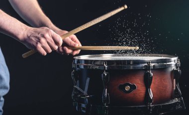 Davulcu davul çubuklarıyla davula vuruyor. Siyah arka planda su sıçratıyor..