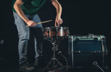 Bir erkek davulcu ve davul seti siyah arka planda, müzisyen çalmaya hazırlanıyor..