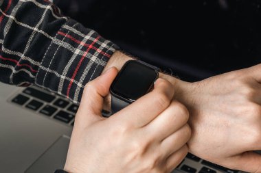 Bir adam akıllı bir saat kullanır. Bilgisayarın bulanık arka planında yakın plan teknolojisi..