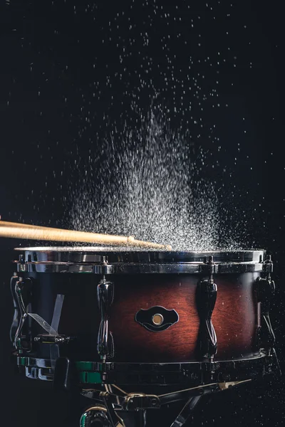 Stock image Drummer using drum sticks hitting snare drum with splashing water on black background.