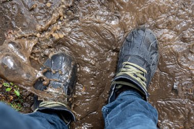Yukarıdan bakıldığında çamurda bir çift yürüyüş ayakkabısı, kot ve bot giyen bir adam yağmurlu havada bataklıkta yürür, kapanır.