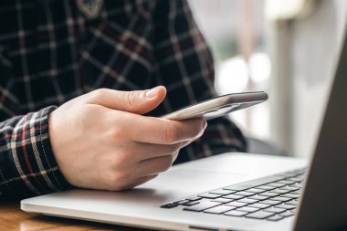 Akıllı telefonu olan bir adam dizüstü bilgisayarda çalışır. Ofiste çalışma konsepti, iş yerinde teknoloji..