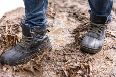 Kot pantolon ve bot giyen bir adam yağmurlu havada, kırsalda, bacakları kapalı bataklıkta yürür..