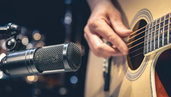 Erkek müzisyen mikrofonun arkasında akustik gitar çalıyor, yakın plan, müzik stüdyosunda kayıt yapıyor..