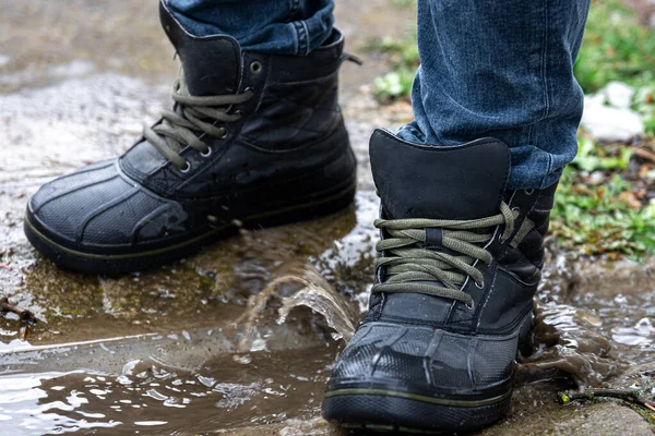 A pair of durable mens boots, a man in quality shoes stands on gravel, quality waterproof boots for bad weather, close-up.