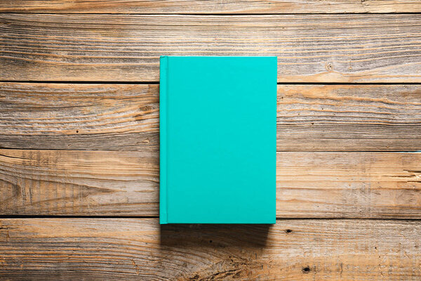 Closed green book on wooden background, top view, copy space.