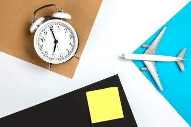 Çalar saat, kâğıt hatırlatma ve renkli kağıt arka planda uçak modeli. Seyahat kavramı.