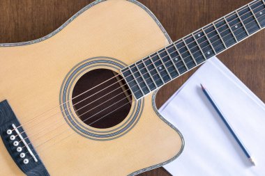 Gitar, kağıt ve kalem. Ahşap bir arka plan, üst manzara, ev müziği konsepti..