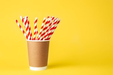 İçecekler için çizgili kağıt kamışlı tek kullanımlık kağıt bardak sarı arka planda izole edilmiş, boşluğu kopyala.