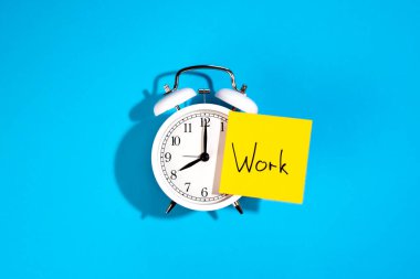 Beyaz alarm saati ve üzerinde yazı olan bir etiket mavi arkaplan, üst görünüm.