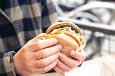 Fast food kafede erkeklerin elinde hamburger, bir adam bir kafede hamburger yiyor, yakın plan..