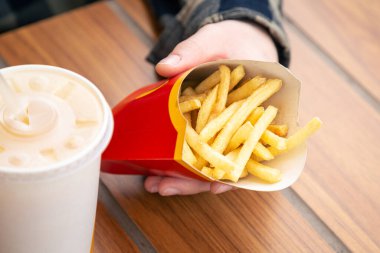 Yakın plan, patates kızartması ve fast food kafede erkeklerin elinde içecek, sağlıksız bir atıştırmalık..