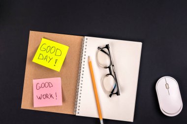 Not defterini, bilgisayar faresini, gözlükleri ve parlak kağıt yapıştırmalarındaki motivasyon yazılarını aç. Ofis işi konsepti, üst görünüm.