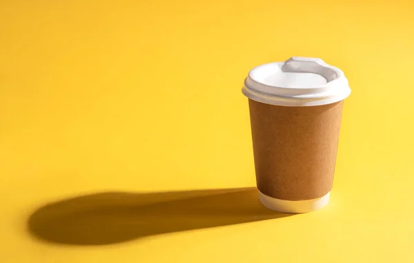 Disposable paper cup with a dark shadow on a yellow background, close-up.