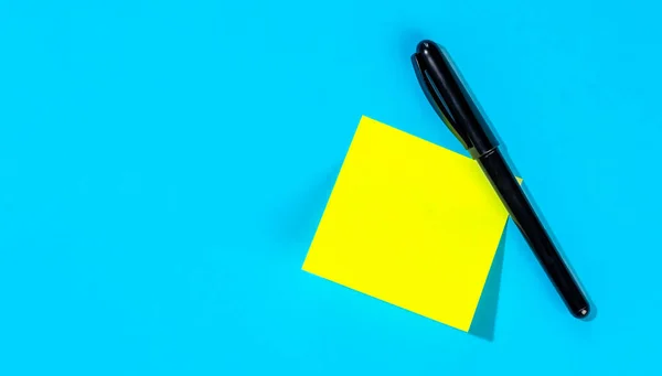 Yellow note with empty place for your text with marker on blue background, flat lay. Reminder concept.
