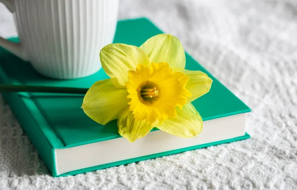 Yellow narcissus flower and a book in a white bed, close-up.