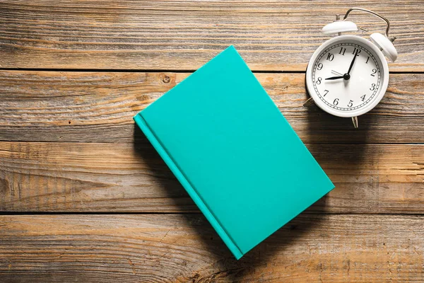 stock image Alarm clock and a blank green book on a wooden background, top view, concept of deadline, study and time organization.