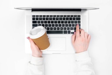 Bir kadın tek kullanımlık bir bardak içkiyle dizüstü bilgisayarda çalışıyor. Minimalist beyaz arkaplan, ofis işi.