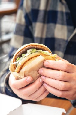 Fast food kafede erkeklerin elinde hamburger, bir adam bir kafede hamburger yiyor, yakın plan..