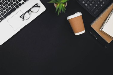 Laptop, kağıt kahve fincanı, siyah zemin üzerinde not defteri ve hesap makinesi, üst görünüm, işyeri, kopyalama alanı.