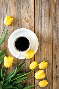 Bir buket parlak sarı lale ve bir fincan koyu kahve ahşap arka planda, üst manzara, kopyalama alanı.