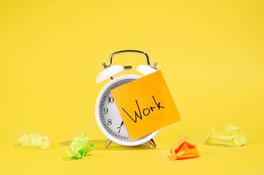 White alarm clock and a sticker with the inscription Work on a yellow background isolated. clipart